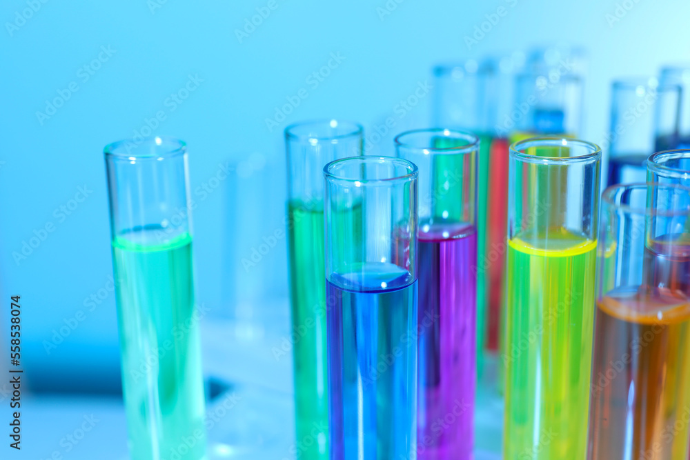 Many test tubes with colorful liquids on blurred background, closeup Many test tubes with colorful liquids on blurred background, closeup
