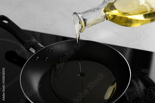 Pouring cooking oil from jug into frying pan on stove, closeup