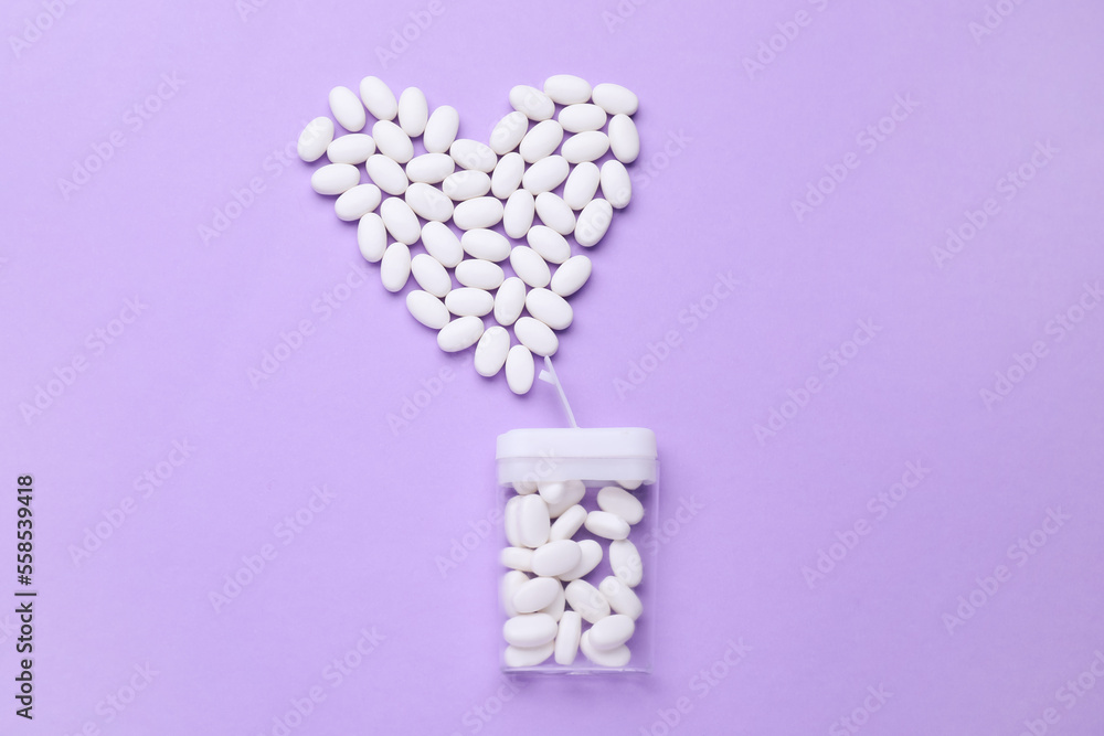Heart made of tasty dragee candies and container on lilac background, flat lay Heart made of tasty dragee candies and container on lilac background, flat lay