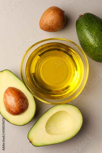 Cooking oil in bowl and fresh avocados on light grey background, flat lay