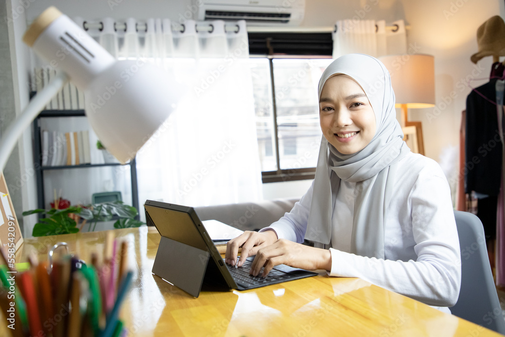 Asian hijab woman using laptop for working in the living room while ...