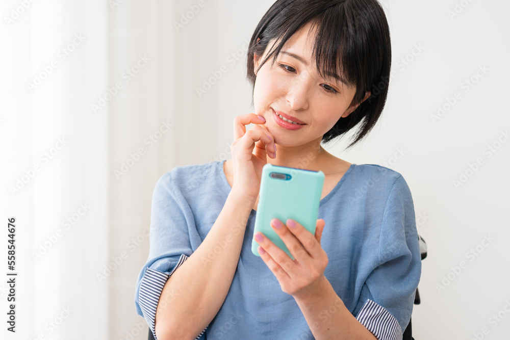 車椅子に座りながらスマートフォンを操作する若い女性 多様性社会イメージ 車椅子に座りながらスマートフォンを操作する若い女性 多様性社会イメージ