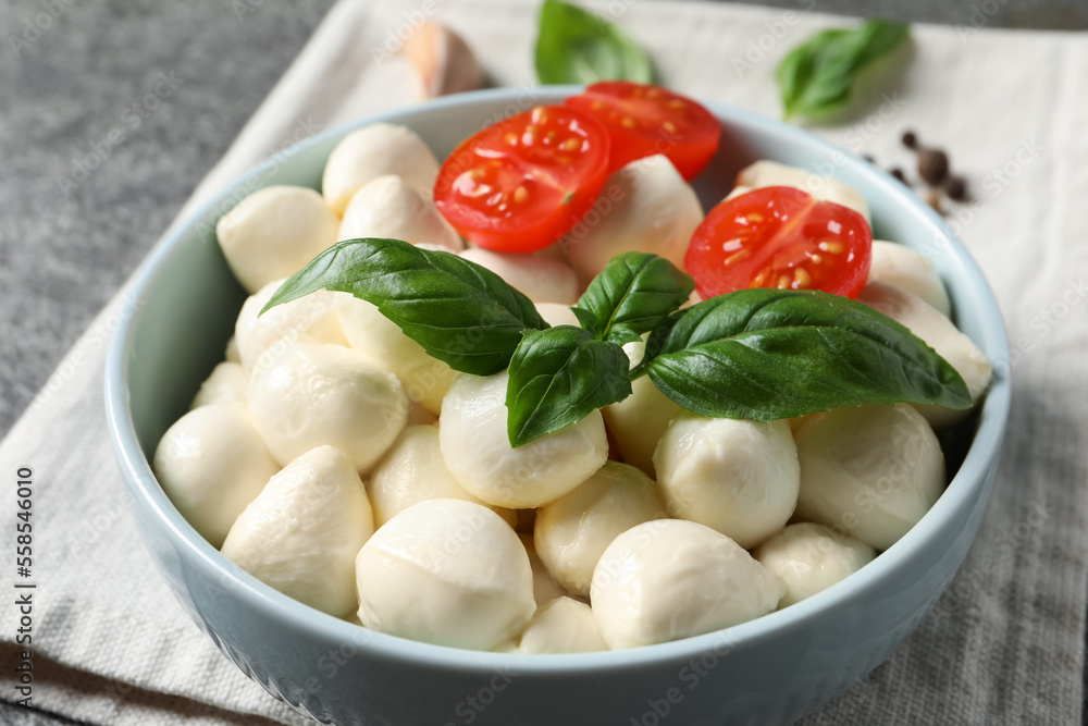 Delicious mozzarella balls, tomatoes and basil leaves in bowl on table, closeup