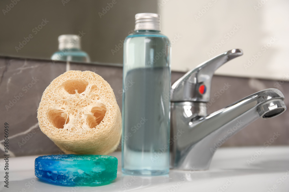 Loofah sponge and cosmetic products on sink in bathroom, closeup Loofah sponge and cosmetic products on sink in bathroom, closeup