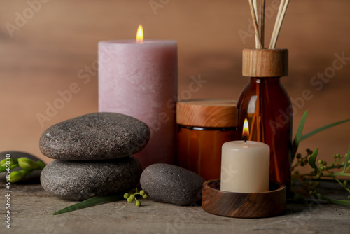 Beautiful spa composition with different care products and burning candles on wooden table, closeup