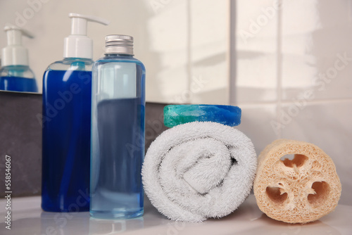 Loofah sponge, rolled towel and cosmetic products on sink in bathroom