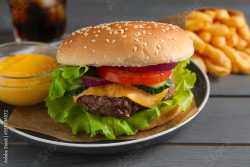 Delicious burger, soda drink and french fries served on grey wooden table, closeup