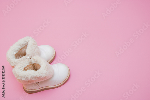 children's white fur boots on a pink background with copy space
