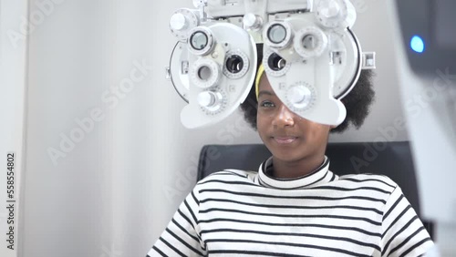 African teen girl Doing Eye Test On Phoropter, African teen girl checking on her eye with optometry machine.
