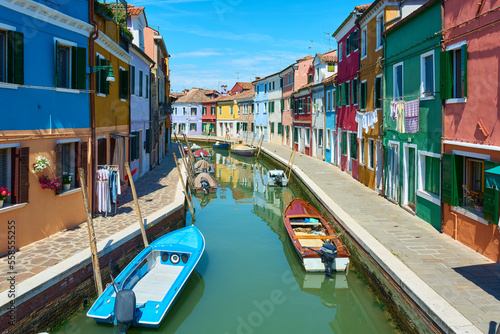 Panoramic view of canal with boats in Burano, Italy, surrounded by picturesque colorful houses decorated with plants, flowers and hanging clothes. © Eduardo Accorinti