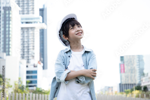Smiling Asian little boy wearing white hard hat and positive thinking for good career. Portrait of a young cheerful construction boy in blue jean clothes. photo