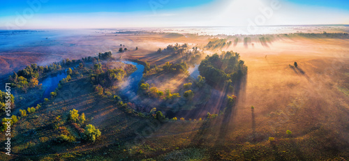 The channel and bends of the river, on a marshy meadow. Orange dry grass, scorched by the summer heat, and morning fog. A wonderful landscape at dawn. Drone view.