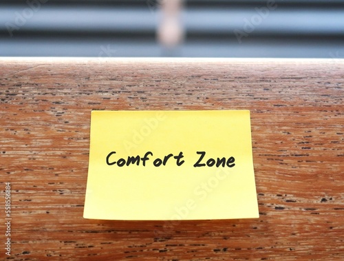 A yellow stick note on the wood background with text written COMFORT ZONE, concept of psychological state to feel at ease and in control, low anxiety and stress, feel safety