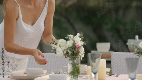 Young woman puts a bouquet of white flowers in a vase on the table for an upcoming event, summer outdoors