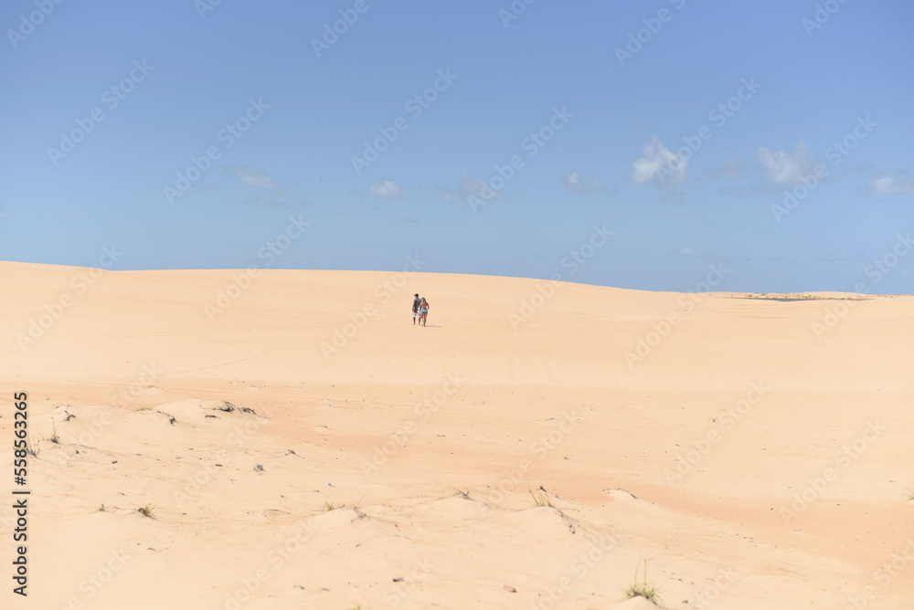 Panoramic view of a couple walking in the distance in the dunes on a sunny blue sky day