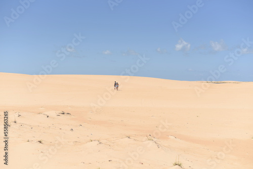Panoramic view of a couple walking in the distance in the dunes on a sunny blue sky day