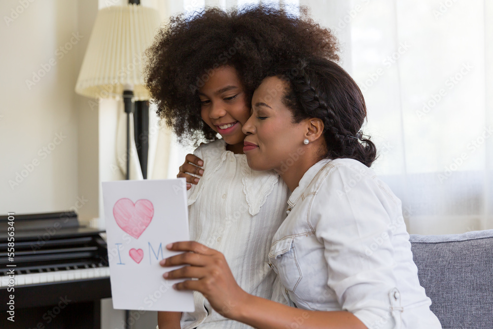 Young mother hugging her daughter and holding happy mother day paper card at home Young mother hugging her daughter and holding happy mother day paper card at home