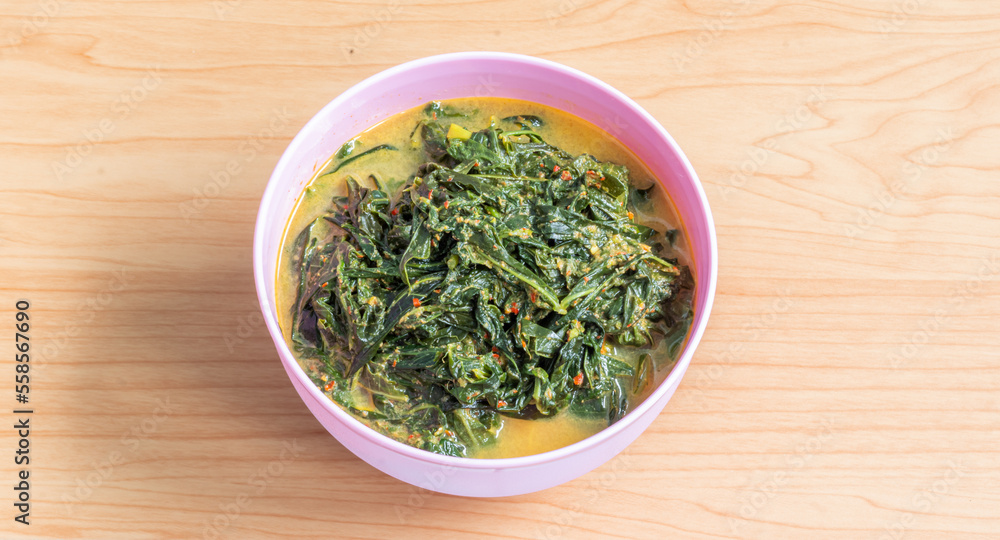 Gulai daun singkong in Minang is indonesian traditional cuisine made from cassava leaves cooked with coconut milk, spices and fried anchovy. Selective focus and blurry selection. Gulai daun singkong in Minang is indonesian traditional cuisine made from cassava leaves cooked with coconut milk, spices and fried anchovy. Selective focus and blurry selection.