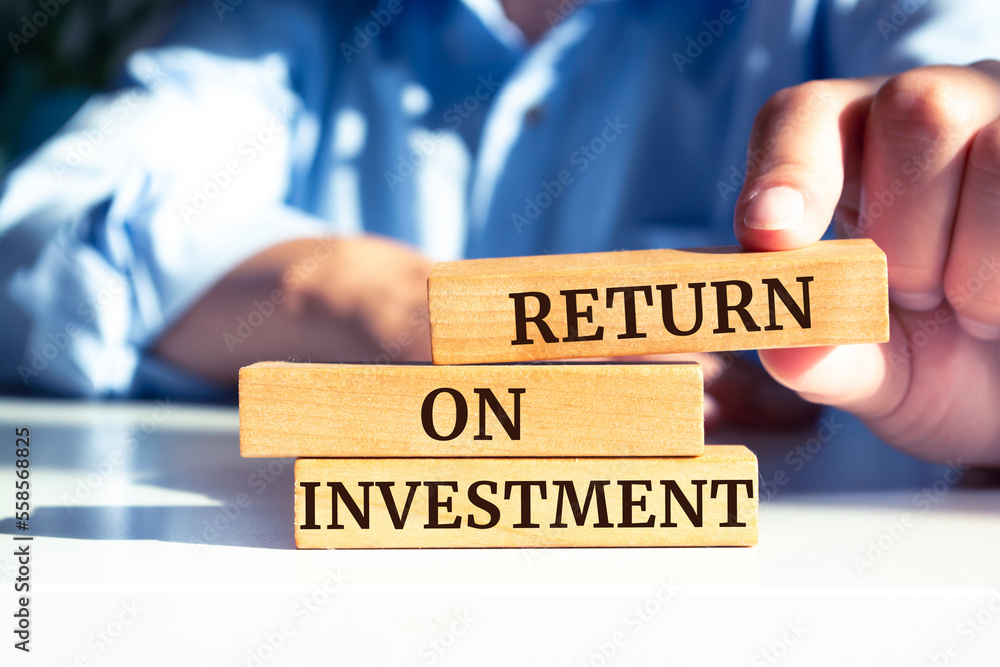 Closeup on businessman holding a wooden blocks with text 'RETURN ON INVESTMENT', business concept Closeup on businessman holding a wooden blocks with text 'RETURN ON INVESTMENT', business concept