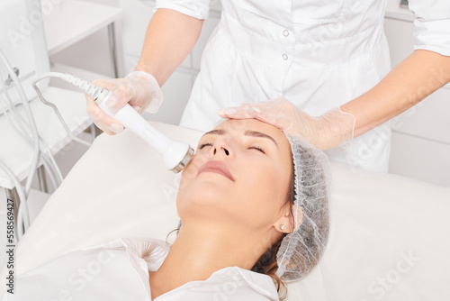 Fotografija Beautician makes ultrasound skin tightening for rejuvenation woman face using phonophoresis, anti aging cosmetic procedure with in beauty spa salon