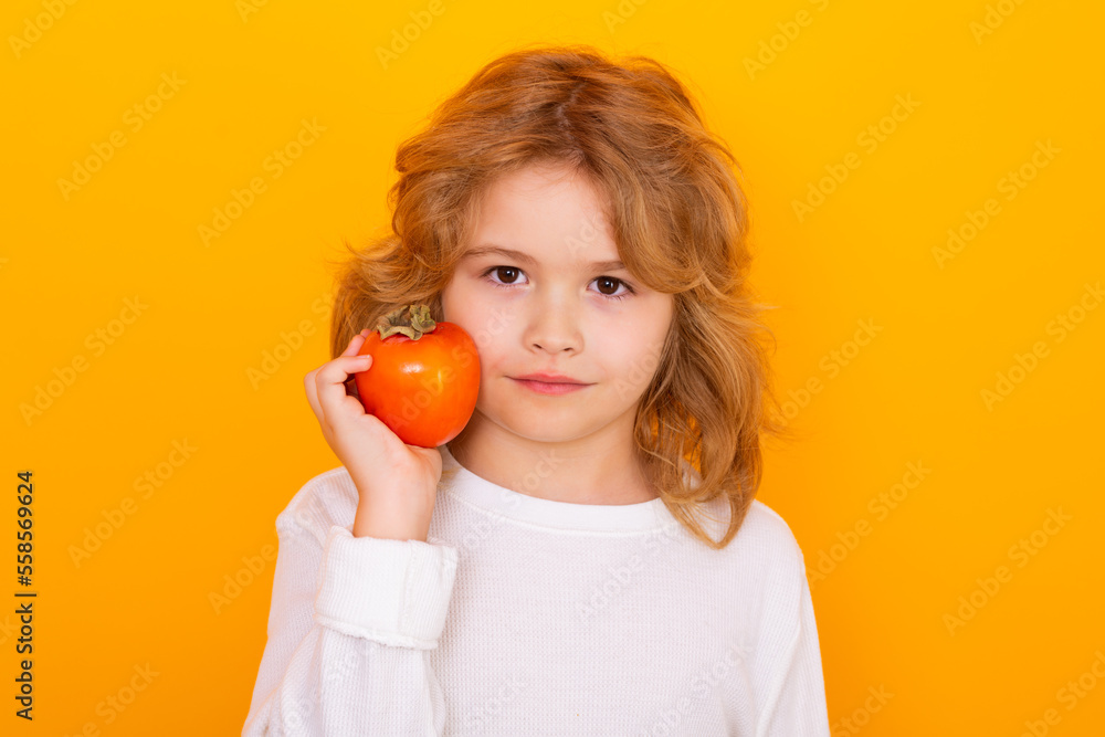 Vitamin and healthy fruits for kids. Kid with persimmon in studio. Studio portrait of cute child hold persimmon isolated on yellow background. Vitamin and healthy fruits for kids. Kid with persimmon in studio. Studio portrait of cute child hold persimmon isolated on yellow background.