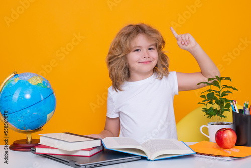 School kid holding index finger up with great new idea. Back to school. Funny little boy from elementary school with book. Portrait of school boy isolated on yellow studio background. Education.
