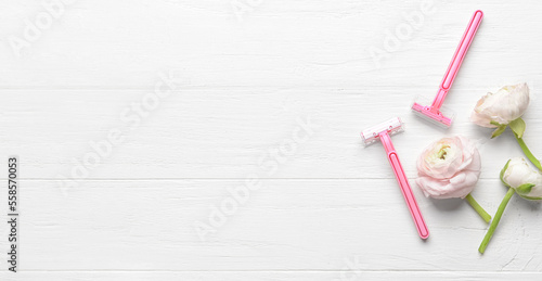 Safety shaving razors and ranunculus flowers on white wooden background with space for text