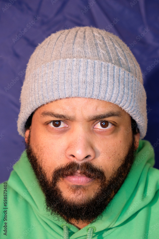 Mixed Race man with beard wearing gray beanie and green hoodie on a blue background with ring light Mixed Race man with beard wearing gray beanie and green hoodie on a blue background with ring light