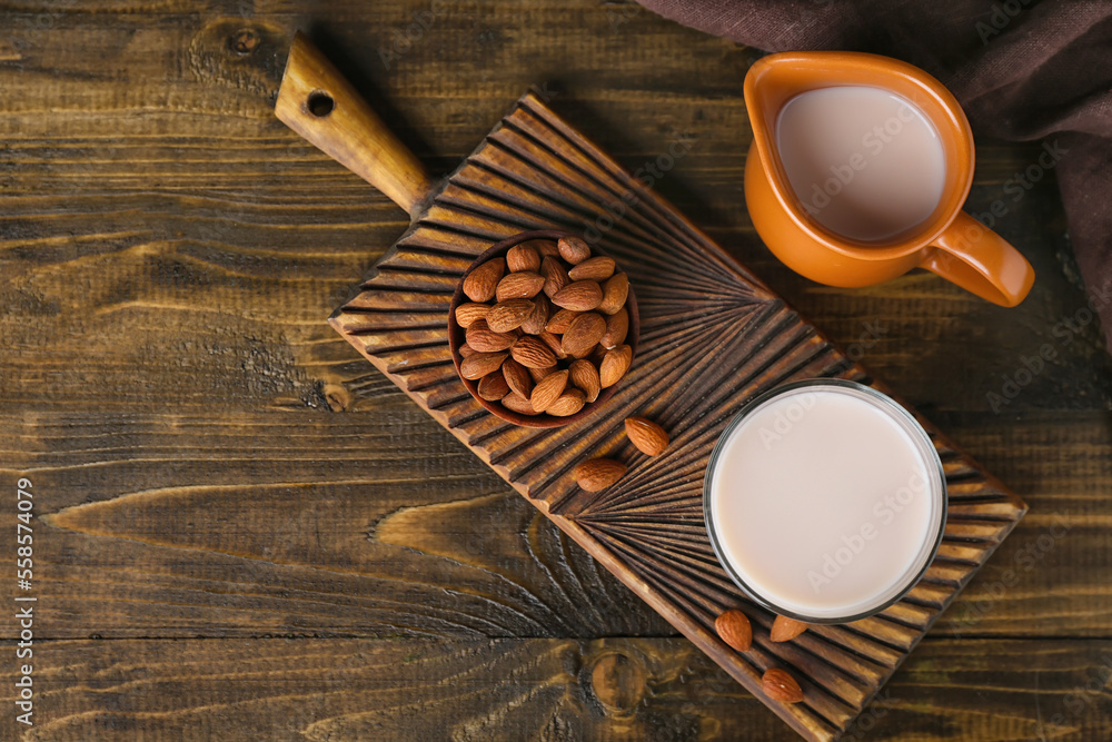 Cutting board with glass of healthy almond milk and nuts on wooden background