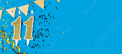 Yellow candle number 11 over blue background. Greeting card with the inscription eleventh birthday. Anniversary or birthday concept. Copy space.