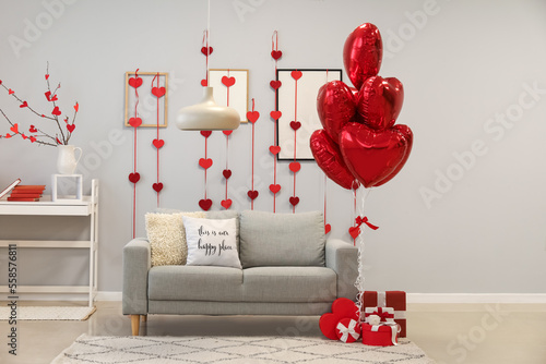 Interior of living room decorated for Valentine's Day with balloons, sofa and gifts