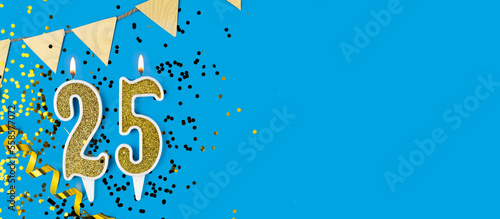 Number 25 gold celebration candle on star and glitter blue background. Copy space.