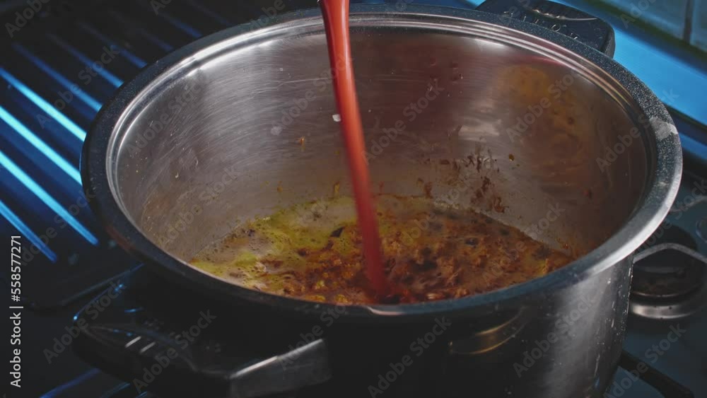 Pouring and stirring tomato sauce with wooden spoon in a grey pot containing vegetables on a stove Pouring and stirring tomato sauce with wooden spoon in a grey pot containing vegetables on a stove