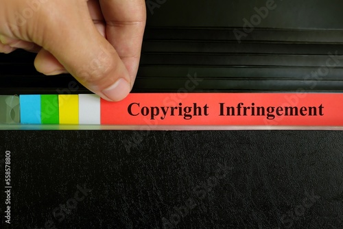 Hand picking copyright infringement file record in black binder folder. Copyright violation business legal concept.	 photo