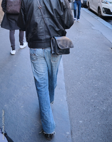 man with black leather jacket and bag blue jeans walking in the city old style 