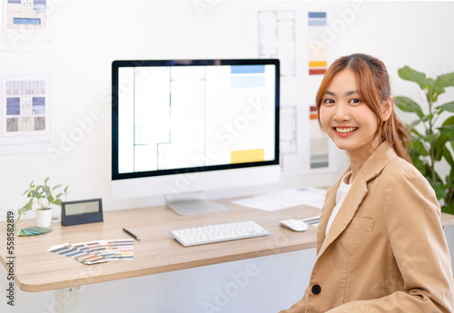 Happy asian woman interior designer sittinging in office working on creative project and smiling. Portrait of cheerful young female architect expressing happy emotions as achieves successful.