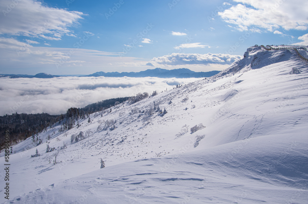 白い雪に覆われた山の斜面。青空と雲と山の遠景。日本の北海道の美幌峠。