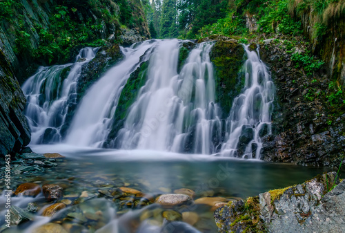 Beautiful mountain rainforest waterfall with fast flowing water and rocks, long exposure. Natural seasonal travel outdoor background with sun shining. Stream waterfall on rocks in the forest © Creatikon Studio