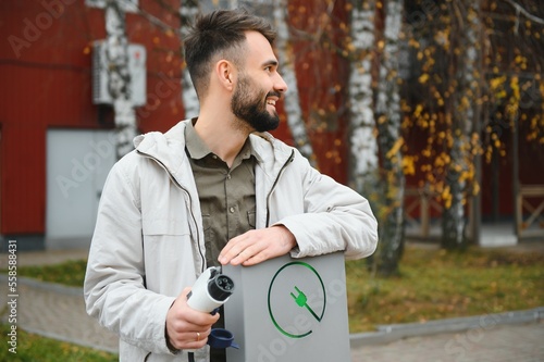 Man holding electric car charger at charging station photo