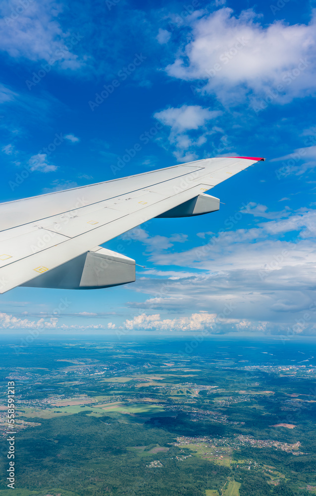 Obraz premium View of airplane wing, blue skies and green land during landing. Airplane window view.