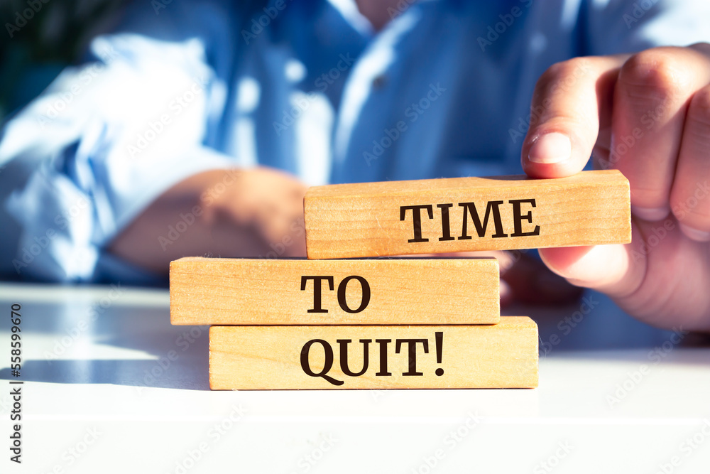 Closeup on businessman holding a wooden blocks with text 'TIME TO QUIT', business concept