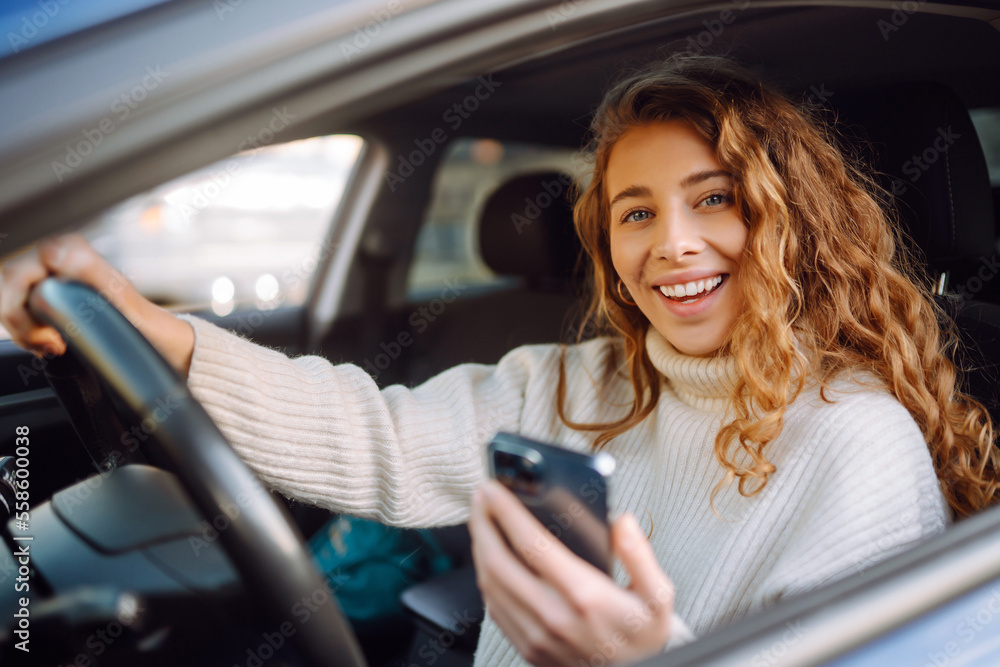 Beautiful young woman is sitting inside a car on the drivers seat with phone. Business, taxi, technologie, internet, online concert. Beautiful young woman is sitting inside a car on the drivers seat with phone. Business, taxi, technologie, internet, online concert.