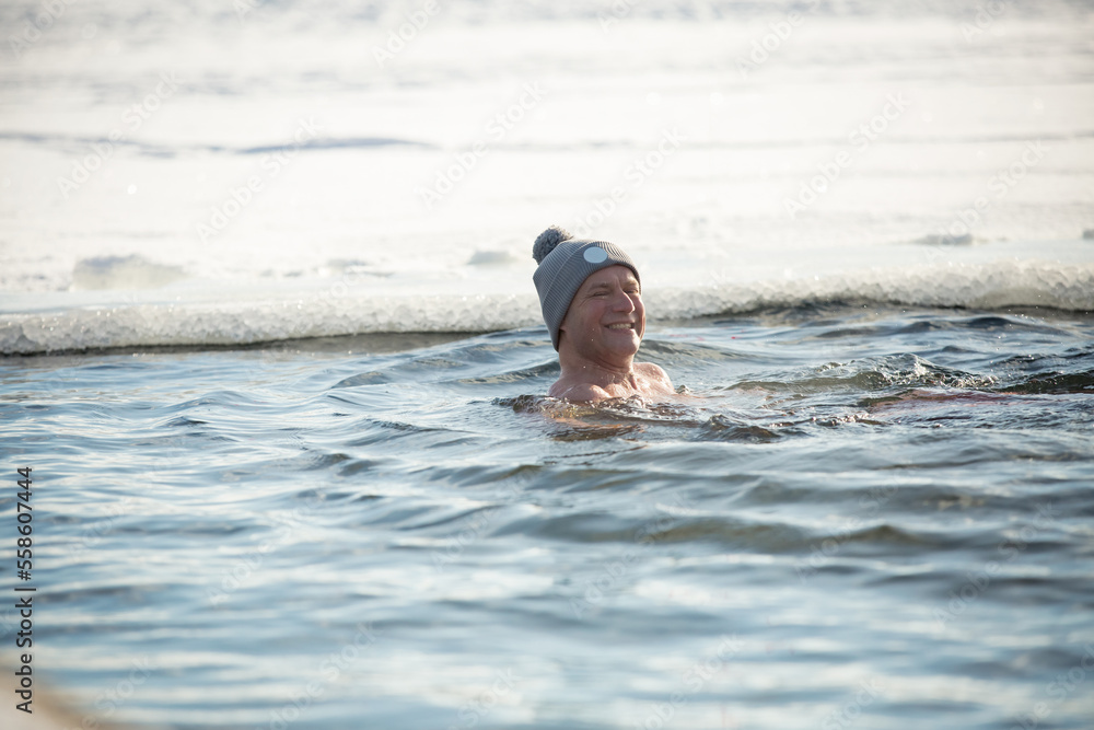 A man in warm hat swimming in an ice hole. Winter activity in Finland. Healthy lifestyle