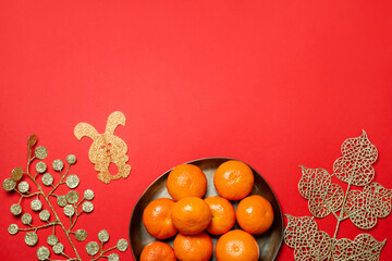 Chinese or lunar new year flat lay with plate of mandarins, paper rabbit as symbol of 2023 and golden flowers on red