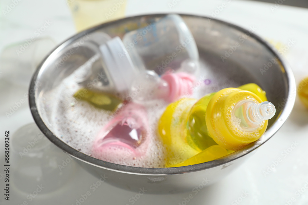 Metal bowl with baby bottles on white table, closeup Metal bowl with baby bottles on white table, closeup