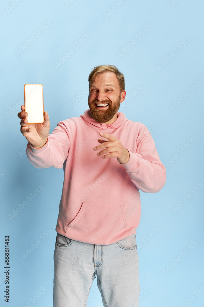Smilling bearded man in casual style clothes showing empty smartphone screen over blue background. Concept of emotions, happiness, ad, sales. Smilling bearded man in casual style clothes showing empty smartphone screen over blue background. Concept of emotions, happiness, ad, sales.