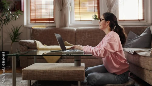 Freelance and remote work. Side view of pretty young woman open laptop. Zoom out. Home office with sofa and windows in background.