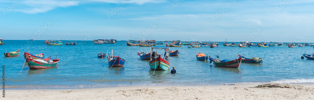 Panorama white sandy beach, calm waves with traditional wooden fishing boat anchored near shoreline in sunny cloud blue sky at Bai Truoc, Vung Tau, Vietnam