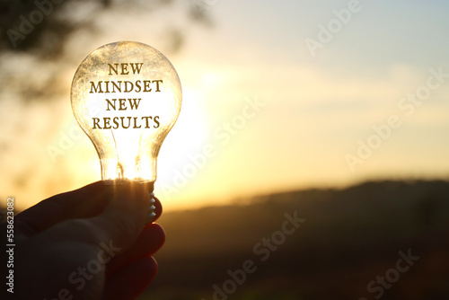 Hand holding light bulb with the text new mindset in front of the bright sun © tomertu