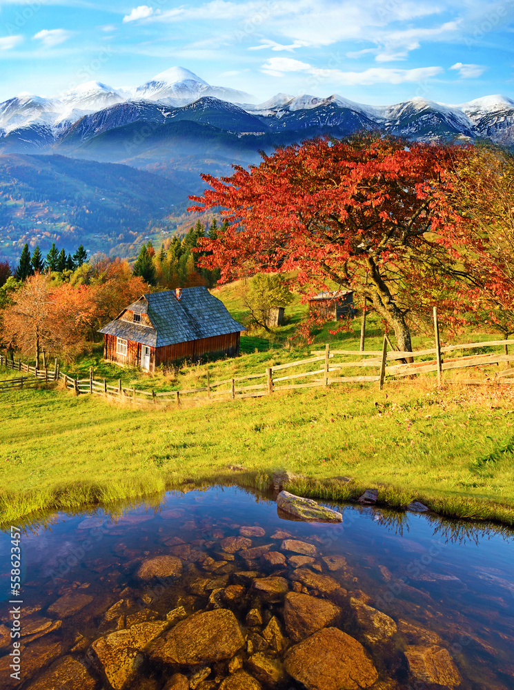 breathtaking view with stones in the pond and hut in the autumn mountains against the background of snow-capped peaks.